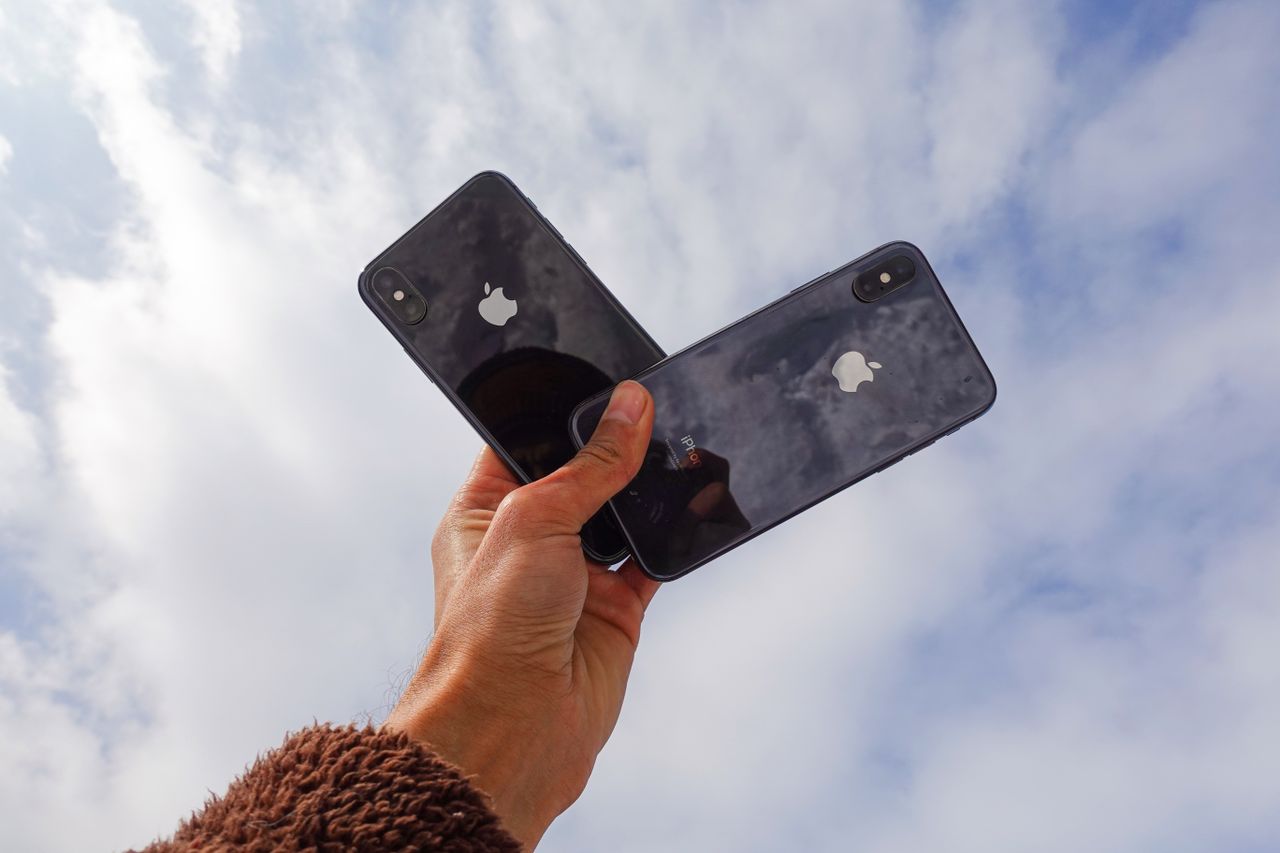 Close-up of a hand holding two smartphones against a cloudy sky, showcasing modern technology.