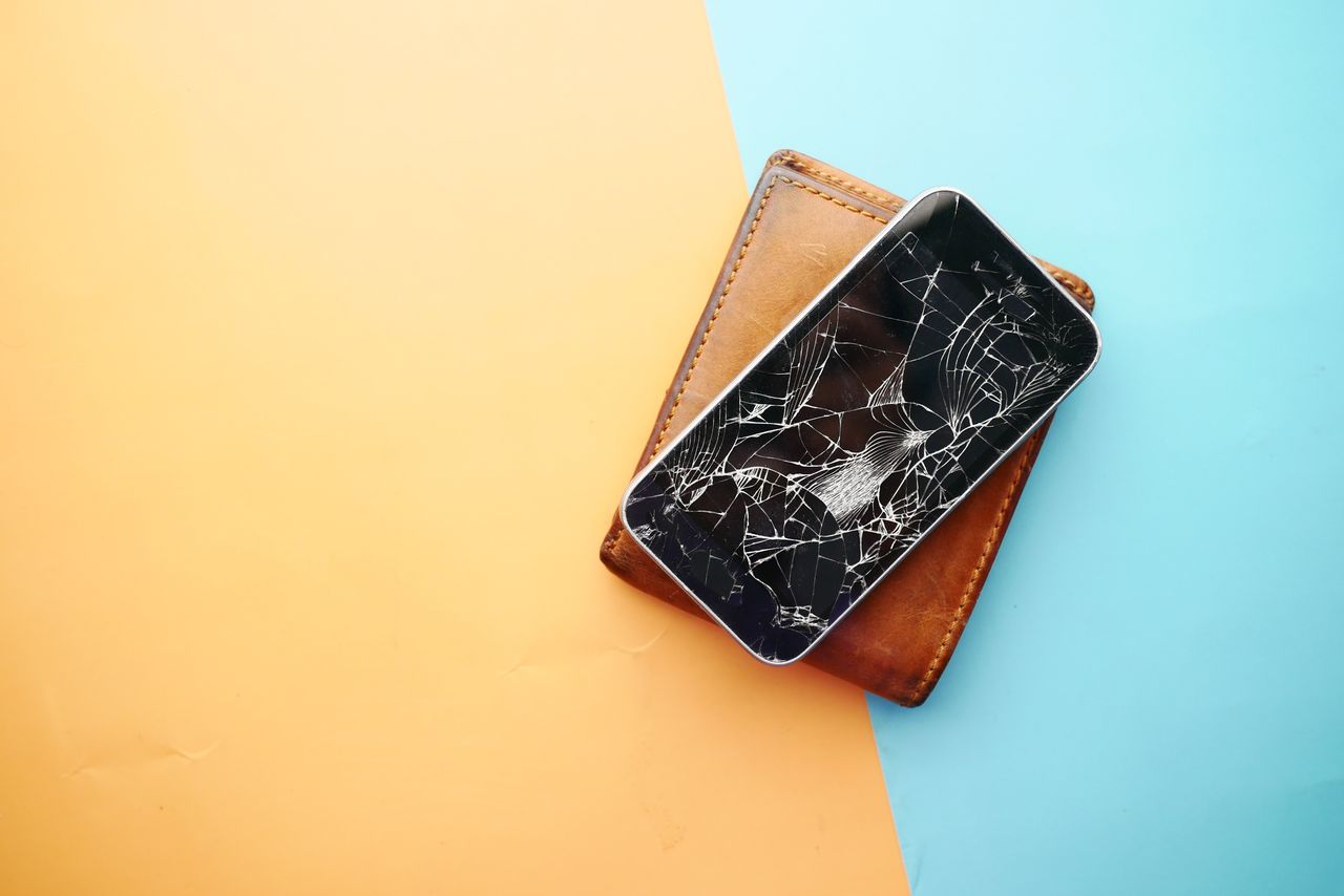 Close-up of a broken smartphone on a wallet, showcasing damaged screen.