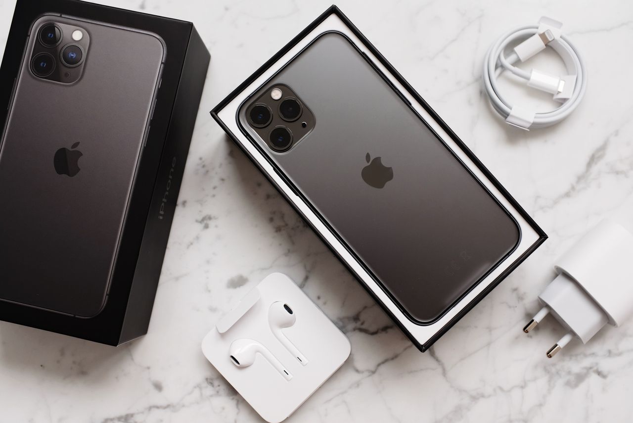 From above composition of black smartphone in box and box top and usb wire and wireless earphones on marble surface